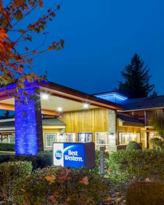 The image shows the exterior of a Best Western hotel, beautifully lit up with blue lights at dusk, surrounded by neatly maintained landscaping and autumn foliage.